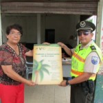 Uniformado junto a ciudadana mostrando el afiche de cprevención de la tala de la palma de cera